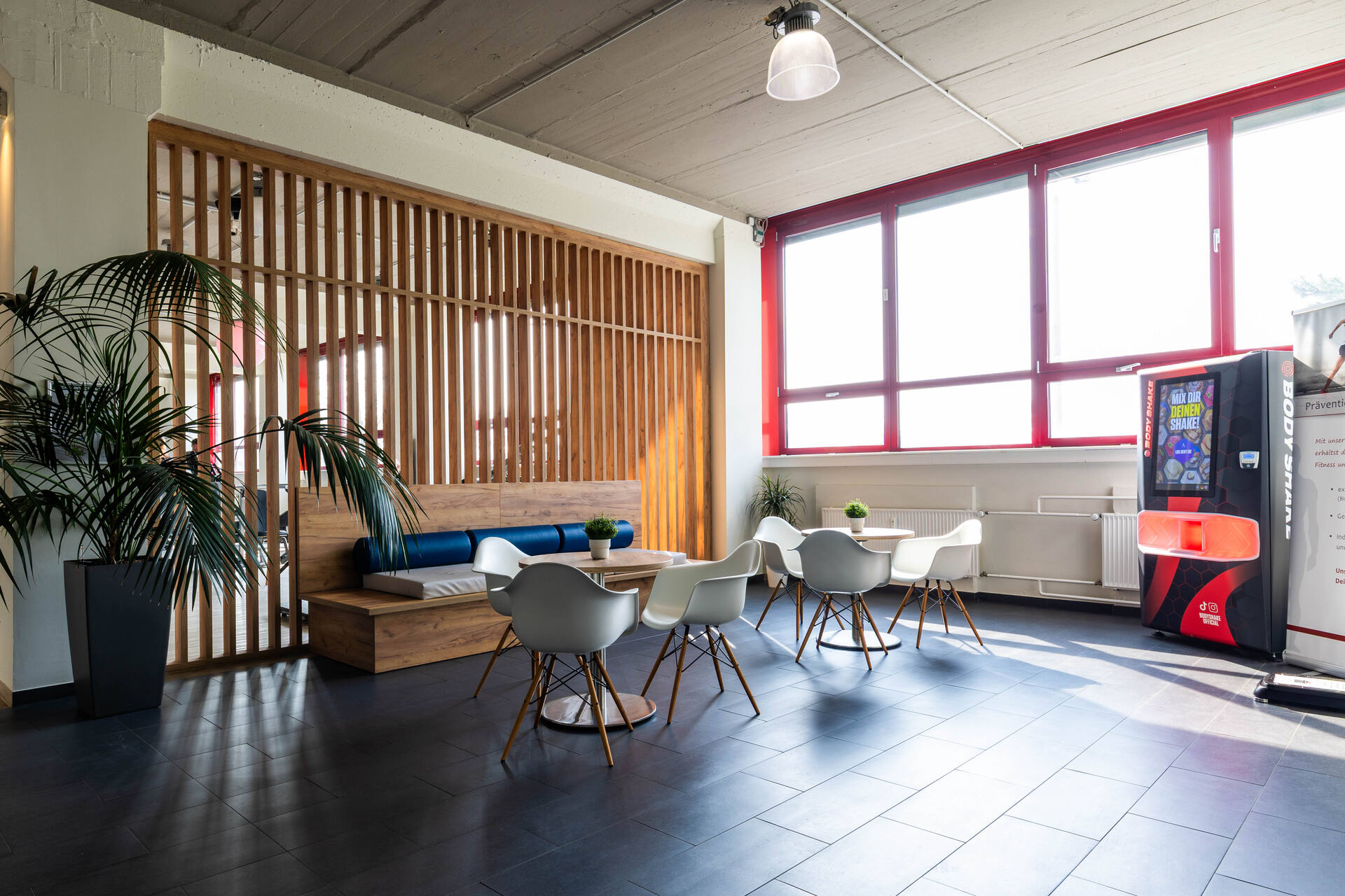 Heller Fitnessstudio-Loungebereich mit Sitzgruppe, großen Fenstern und Automat